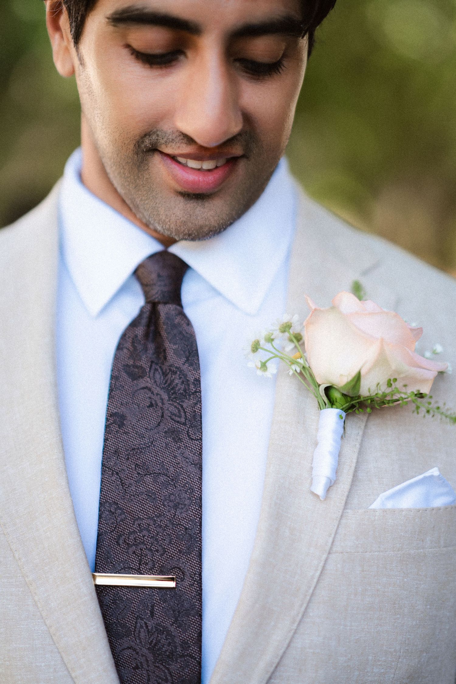 Close-up of a beige suit with paisley tie and pink rose boutonniere.