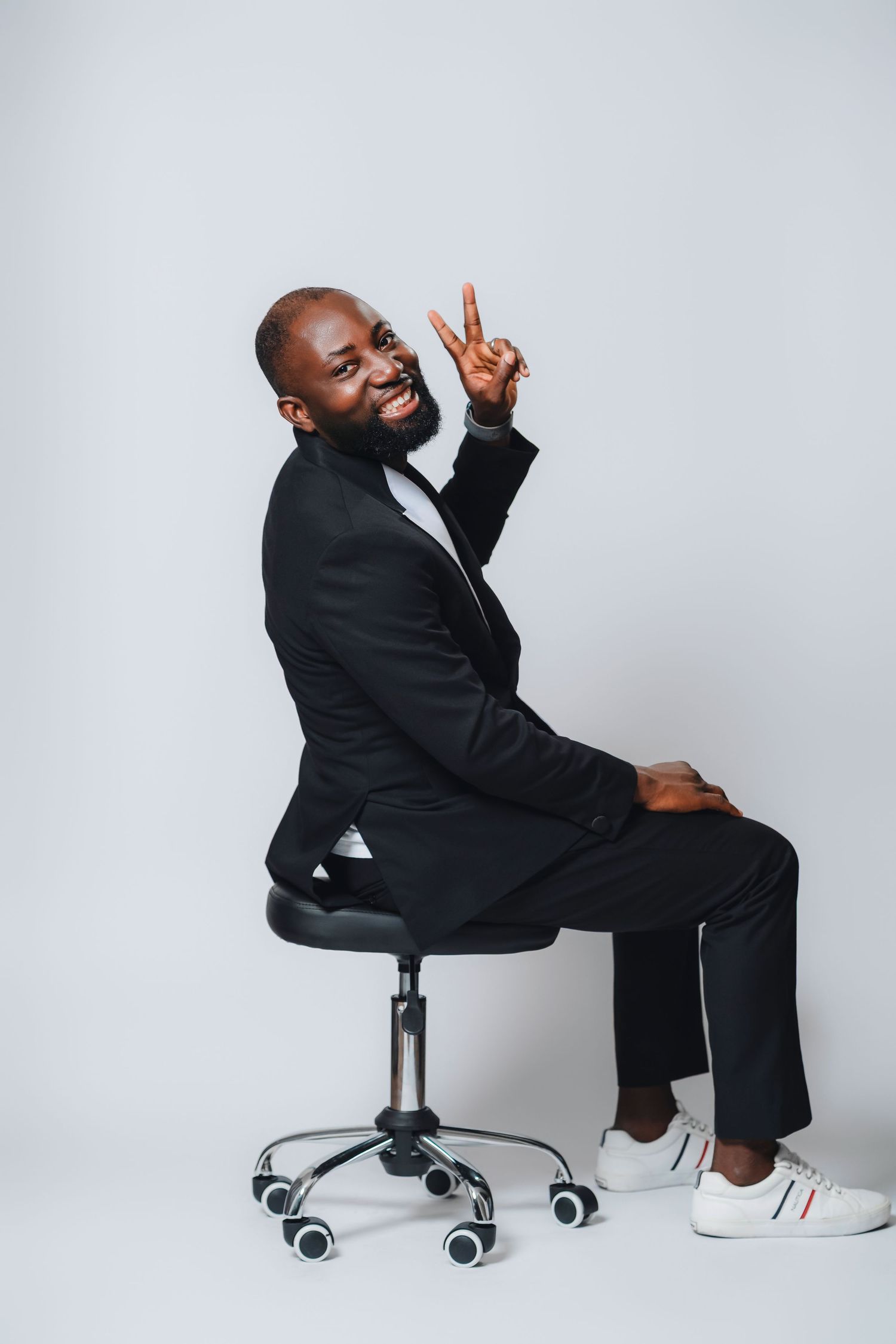 A person in a black suit sits and poses on an office chair against a white backdrop in multiple positions.