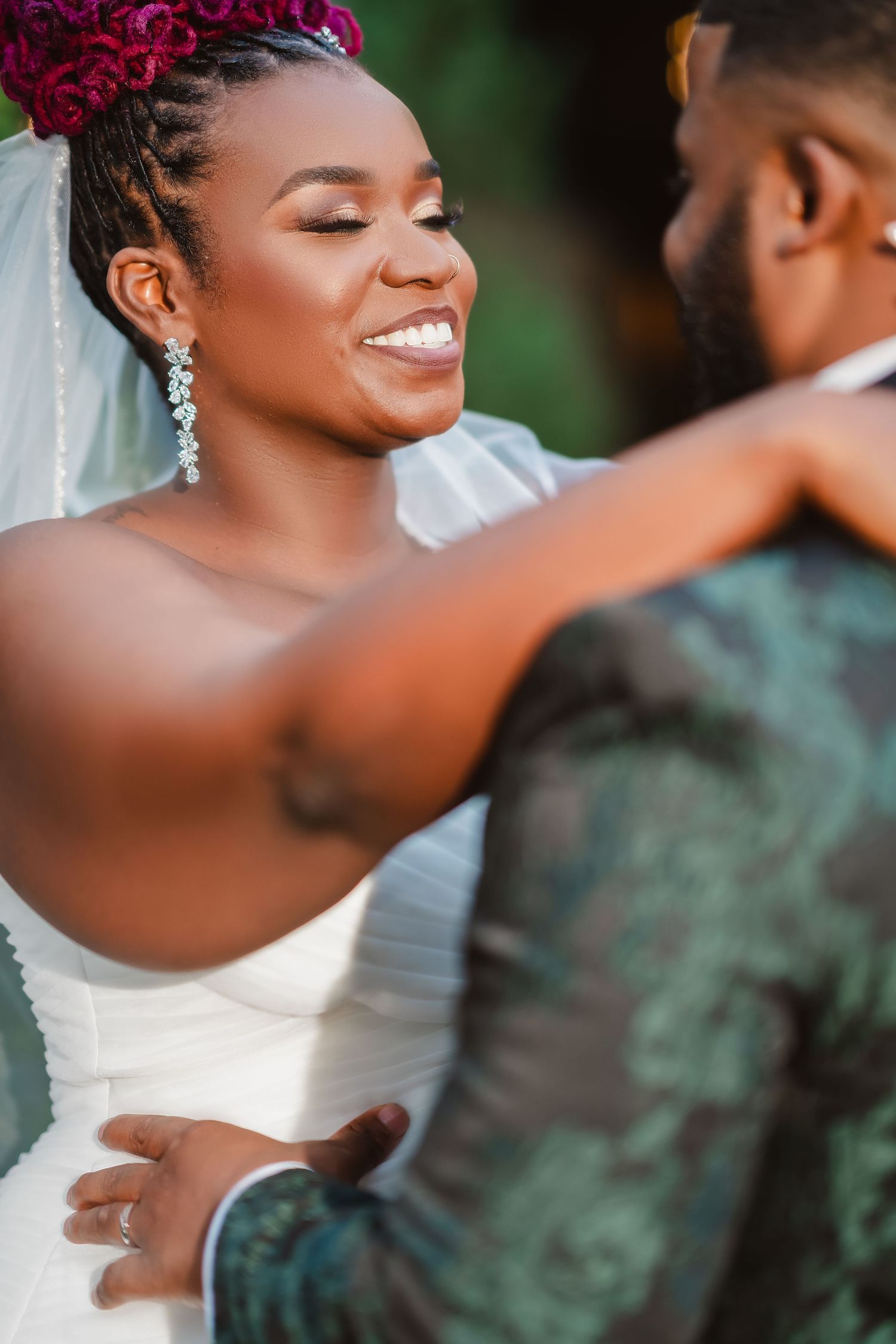 Intimate wedding portrait showing bride in white dress with pink floral hair accessory embracing groom.