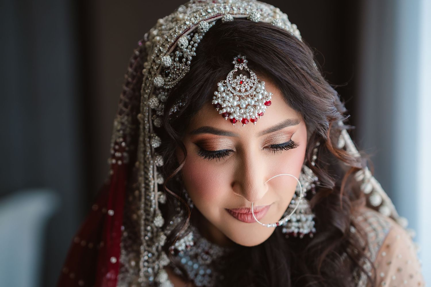 Traditional South Asian bridal jewelry and makeup details with ornate silver headpiece and red accents.