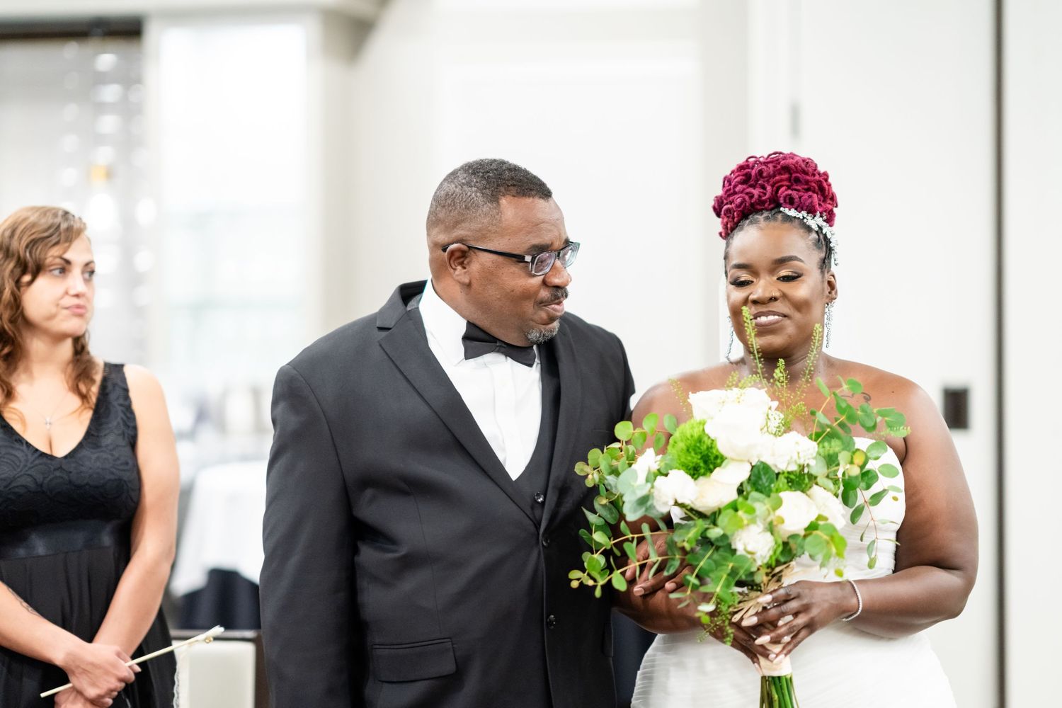 Wedding ceremony guests and attendants gathered in a bright white venue space.
