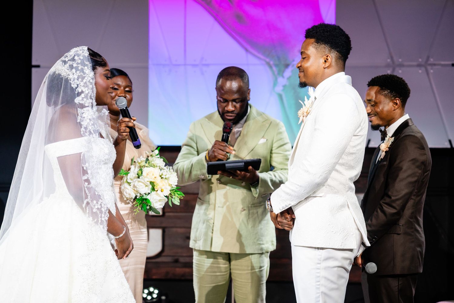 A wedding ceremony takes place on stage with purple lighting and floral decorations.