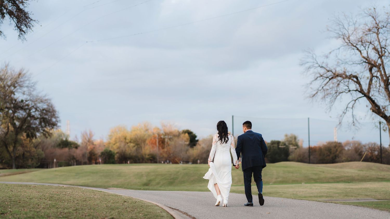 A couple walks hand in hand along a winding path through a scenic park during autumn.