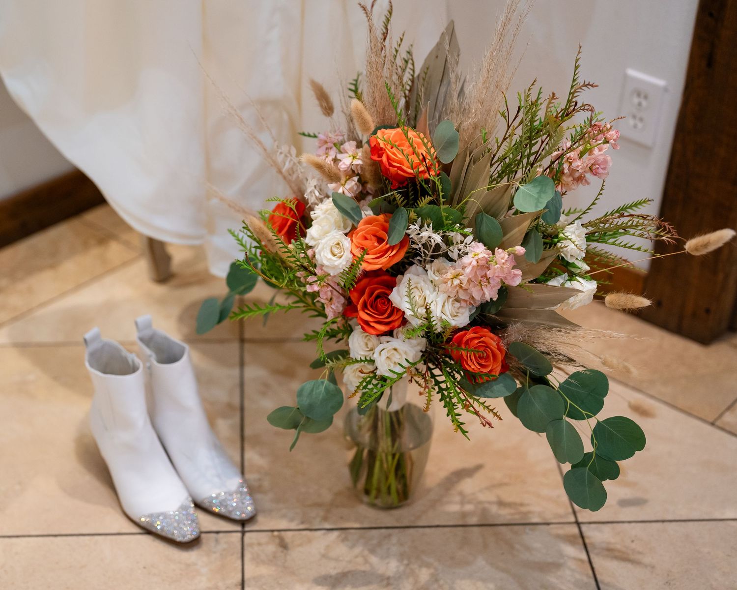 Wedding details showing bridal shoes and coral floral bouquet arrangements on tile floor.
