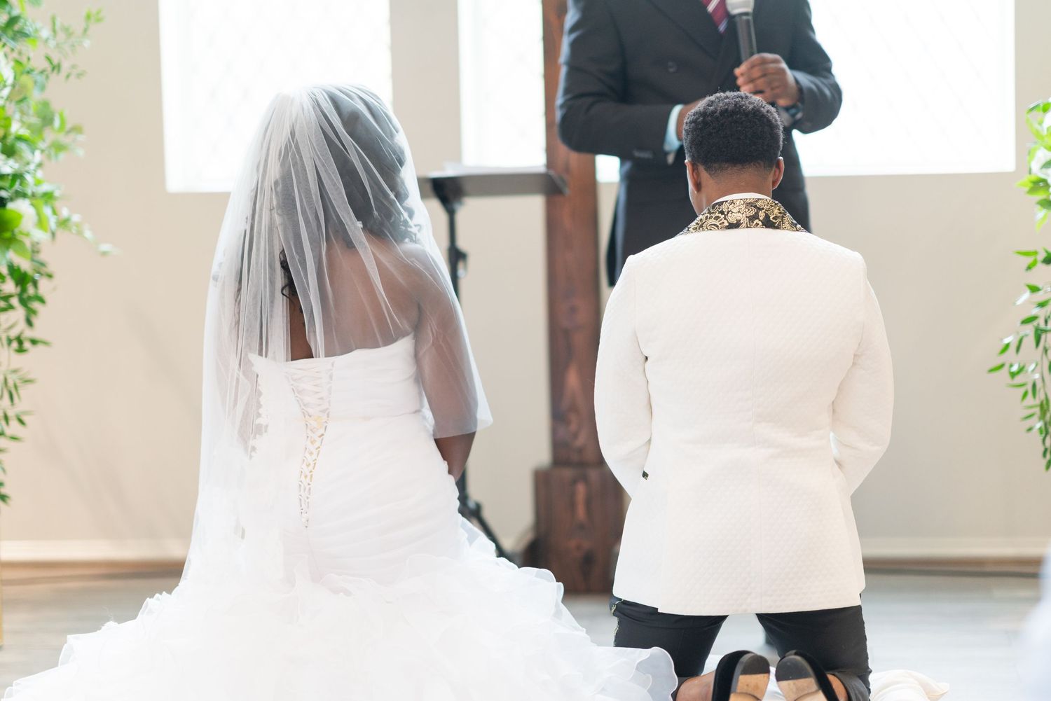 Elegant white wedding ceremony setup with hanging greenery and natural light.