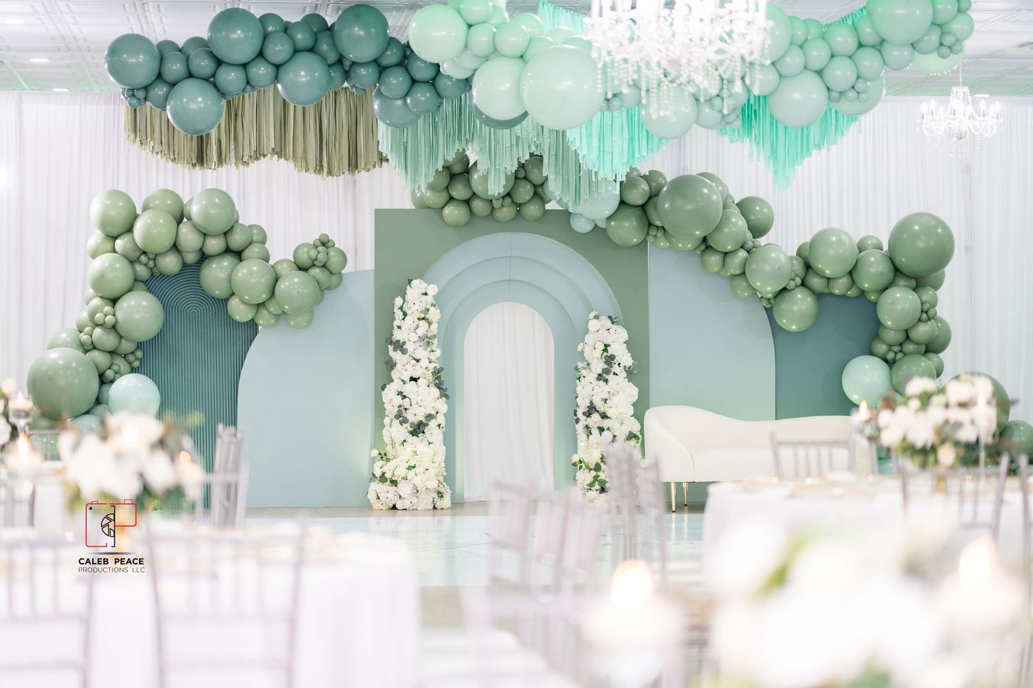 Elegant wedding venue decorated with sage green balloon garlands and white floral arrangements creates a dreamy atmosphere.
