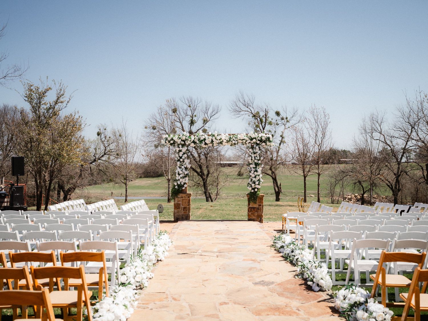 Wooden chairs lined up for an outdoor wedding ceremony with white floral decorations.