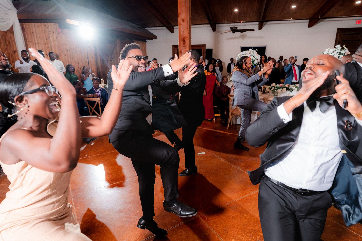 Wedding reception guests dancing enthusiastically on wooden dance floor.