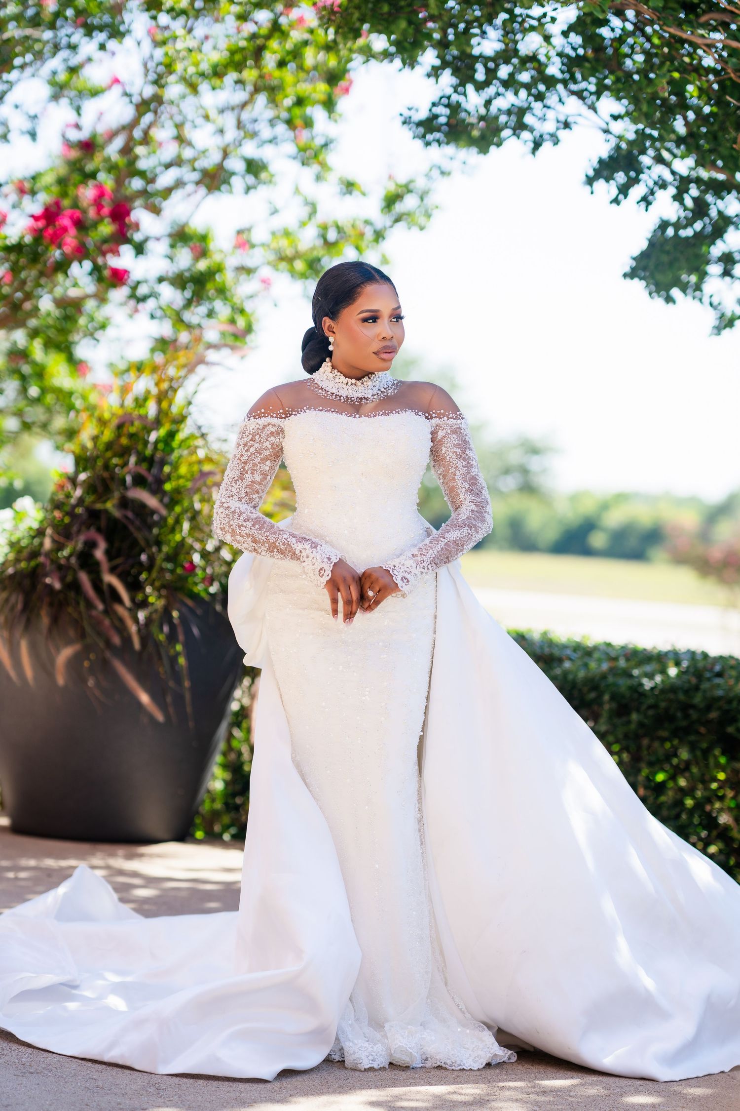 Stunning white wedding gown with lace details photographed against garden backdrop with pink flowers.