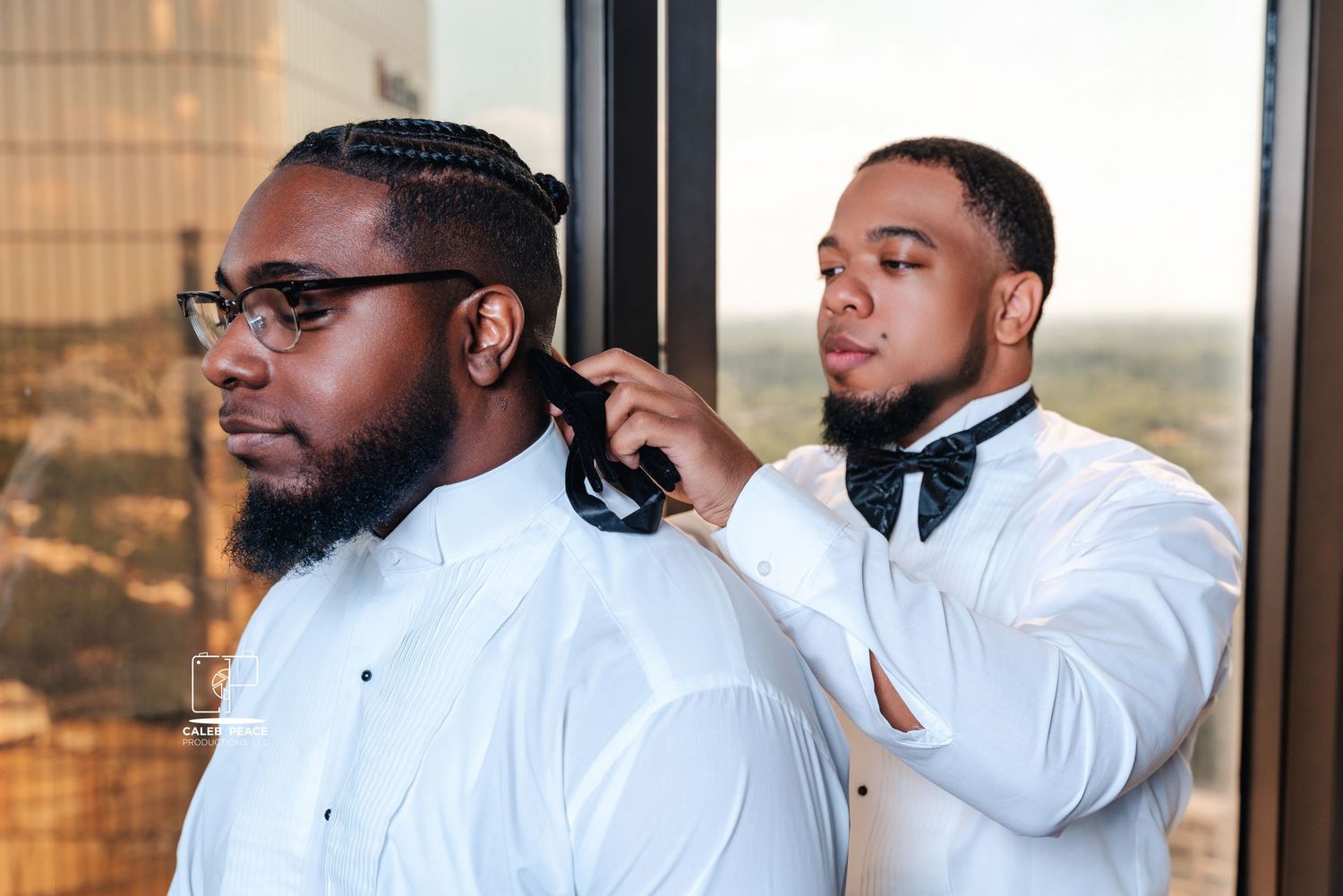 A groomsman helps adjust another's bow tie while getting ready.