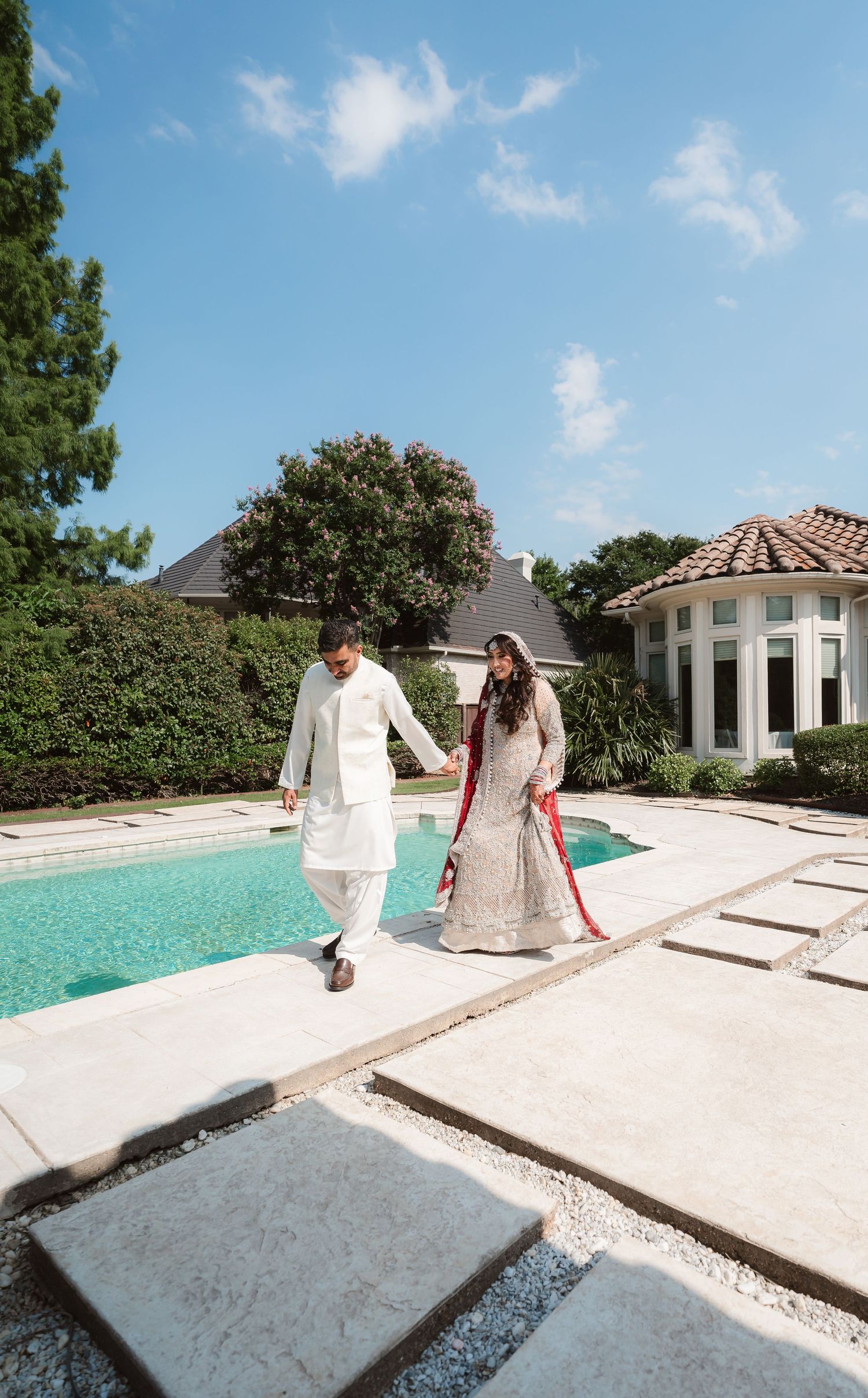 A poolside wedding photoshoot with a couple in traditional attire against a bright blue sky.