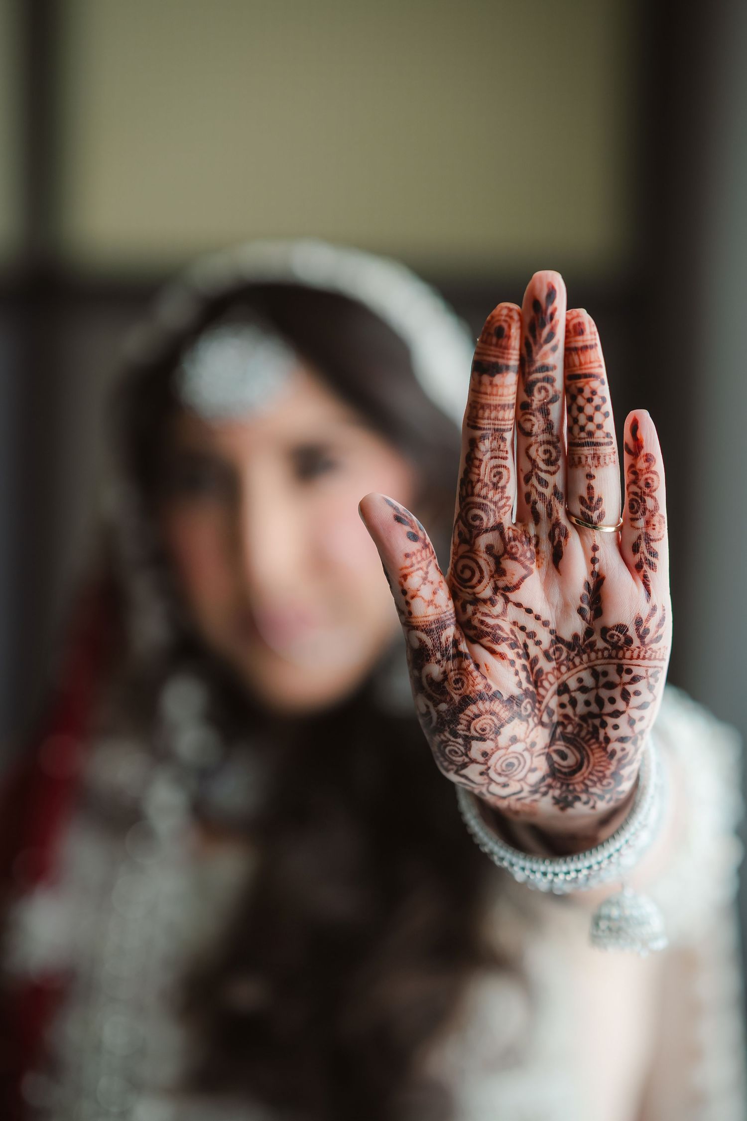 Intricate henna designs displayed on hands against a white traditional wedding dress.