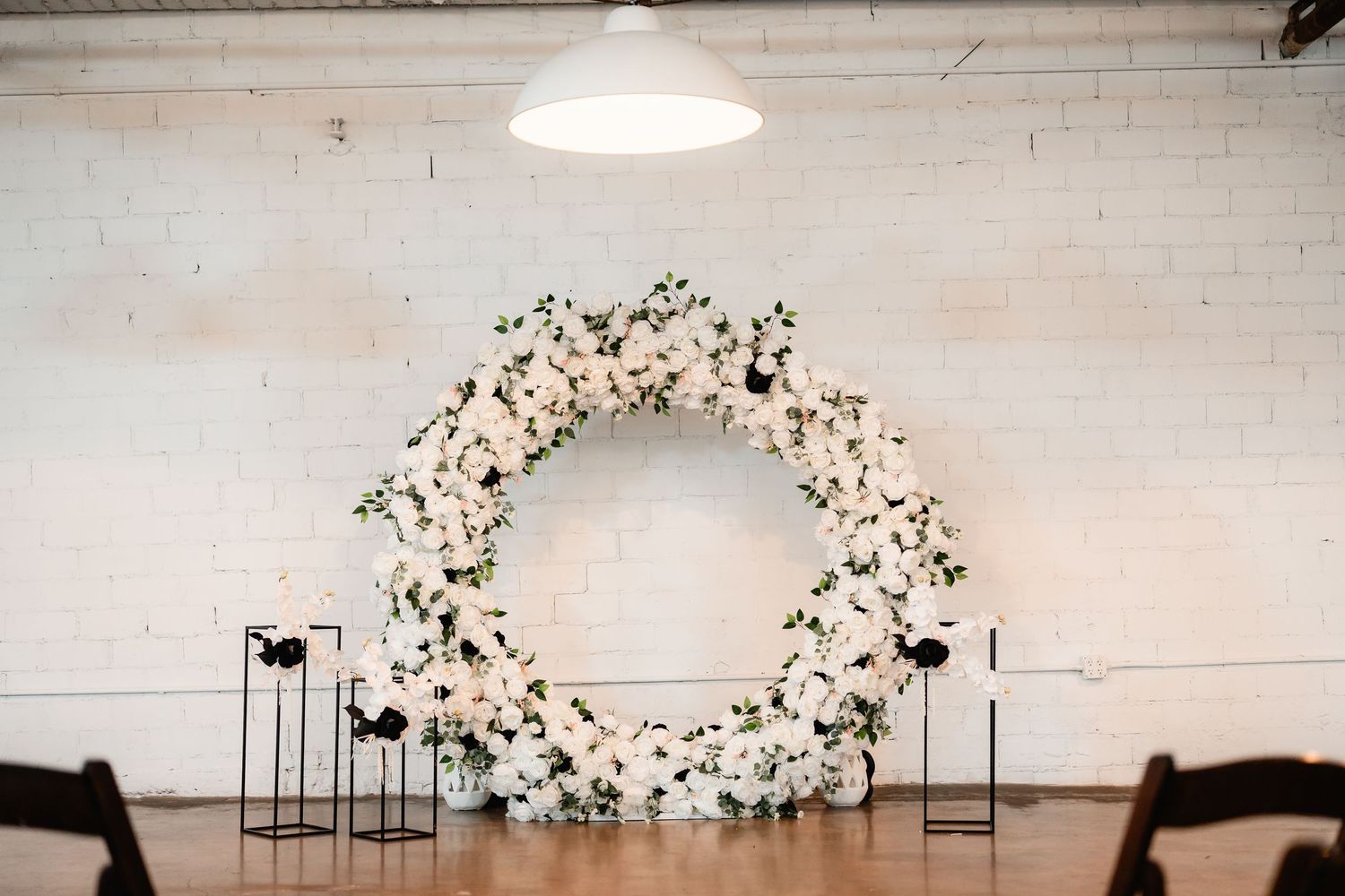 White floral arch installation against white brick wall creates elegant wedding ceremony backdrop.