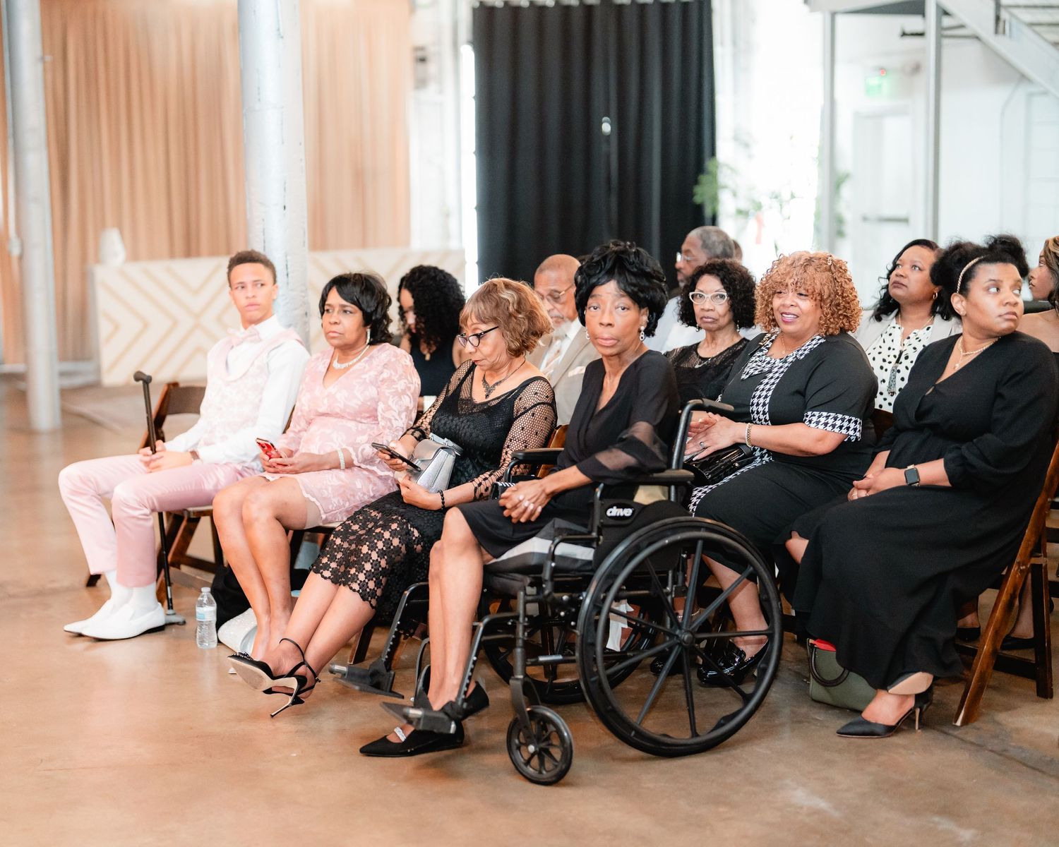 Wedding guests seated in rows including elderly and wheelchair attendees at indoor ceremony.