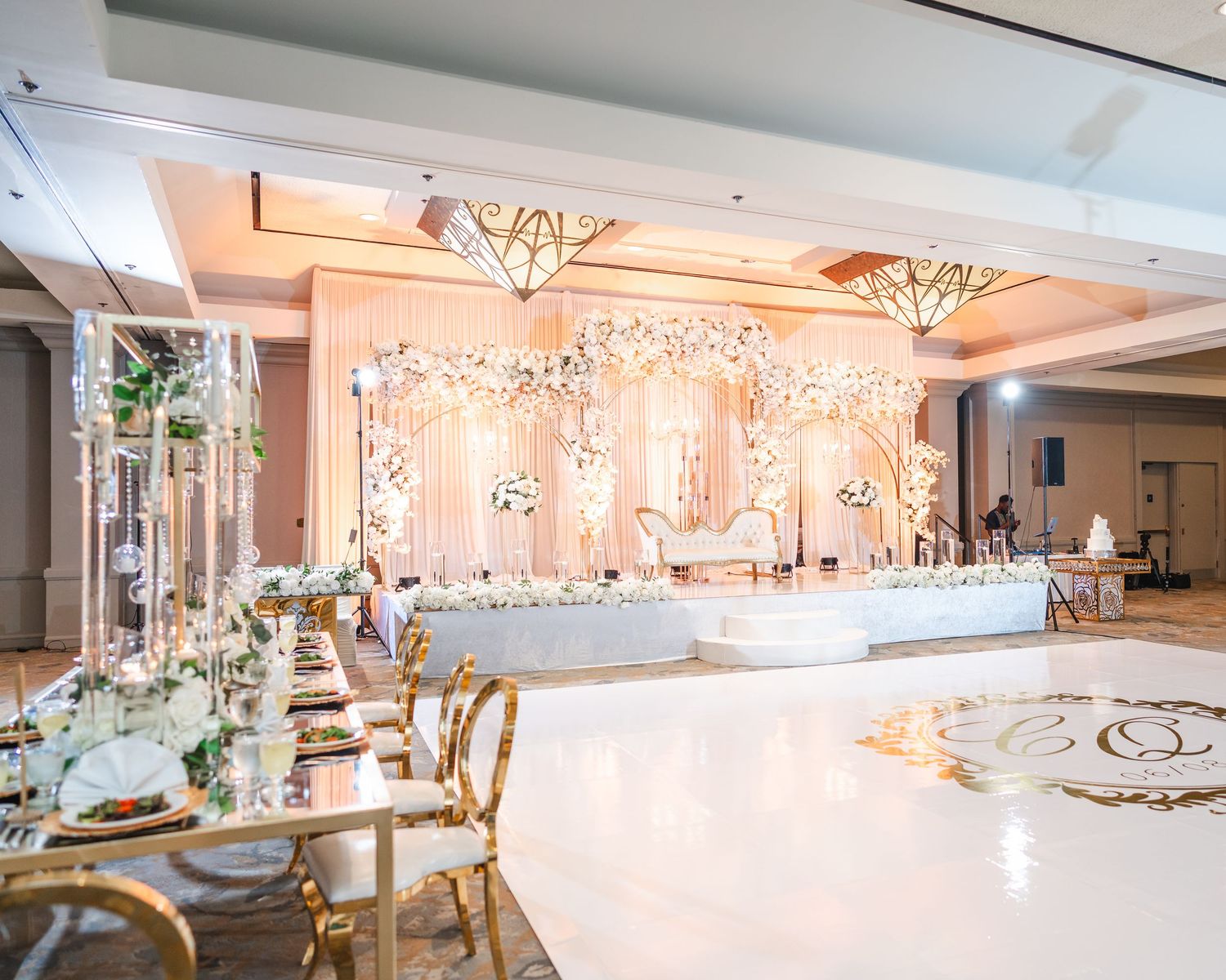 An elegant white and gold wedding reception ballroom with crystal chandeliers and decorative lighting.