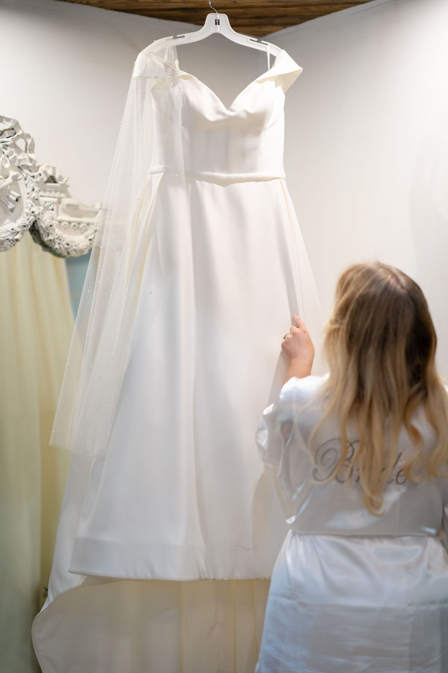 White wedding dress hanging on display in a dressing room with other gowns.