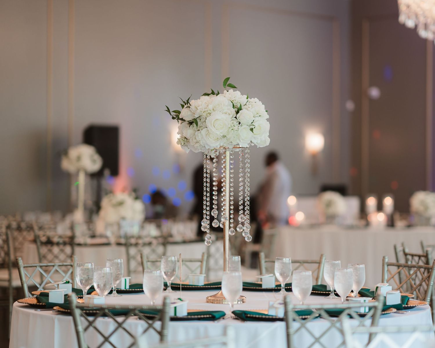 Elegant wedding reception tables decorated with white floral centerpieces and crystal chandeliers in a modern ballroom.