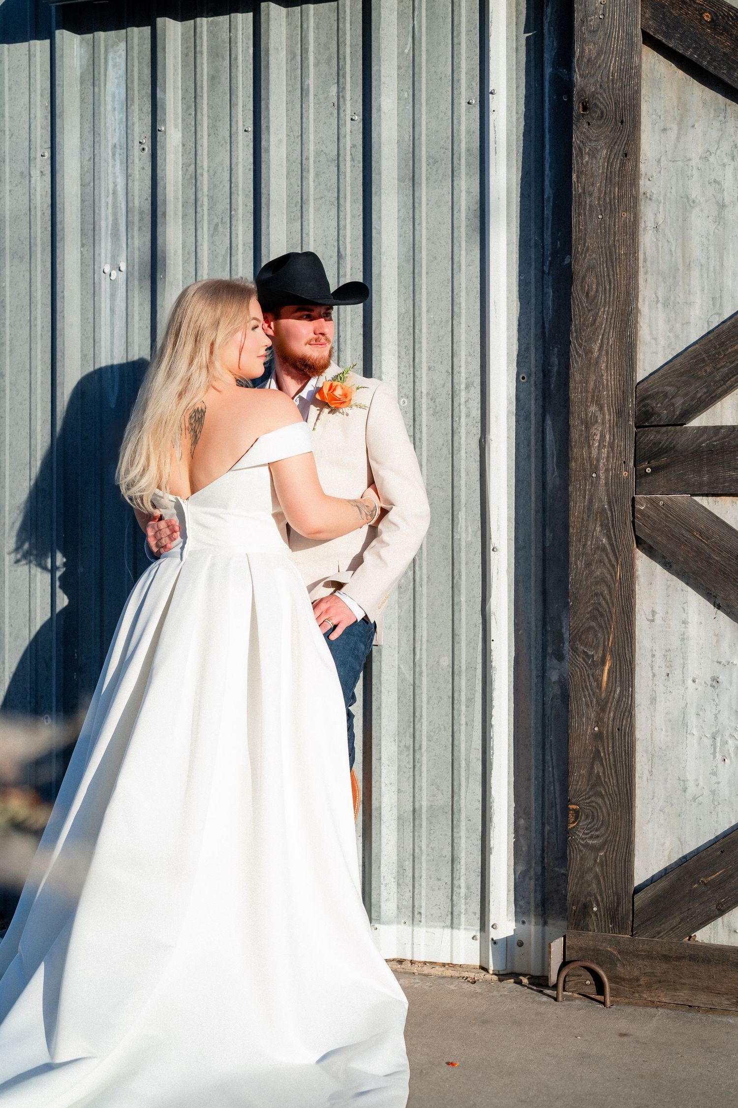 A wedding couple poses against a metal wall in western-inspired attire.