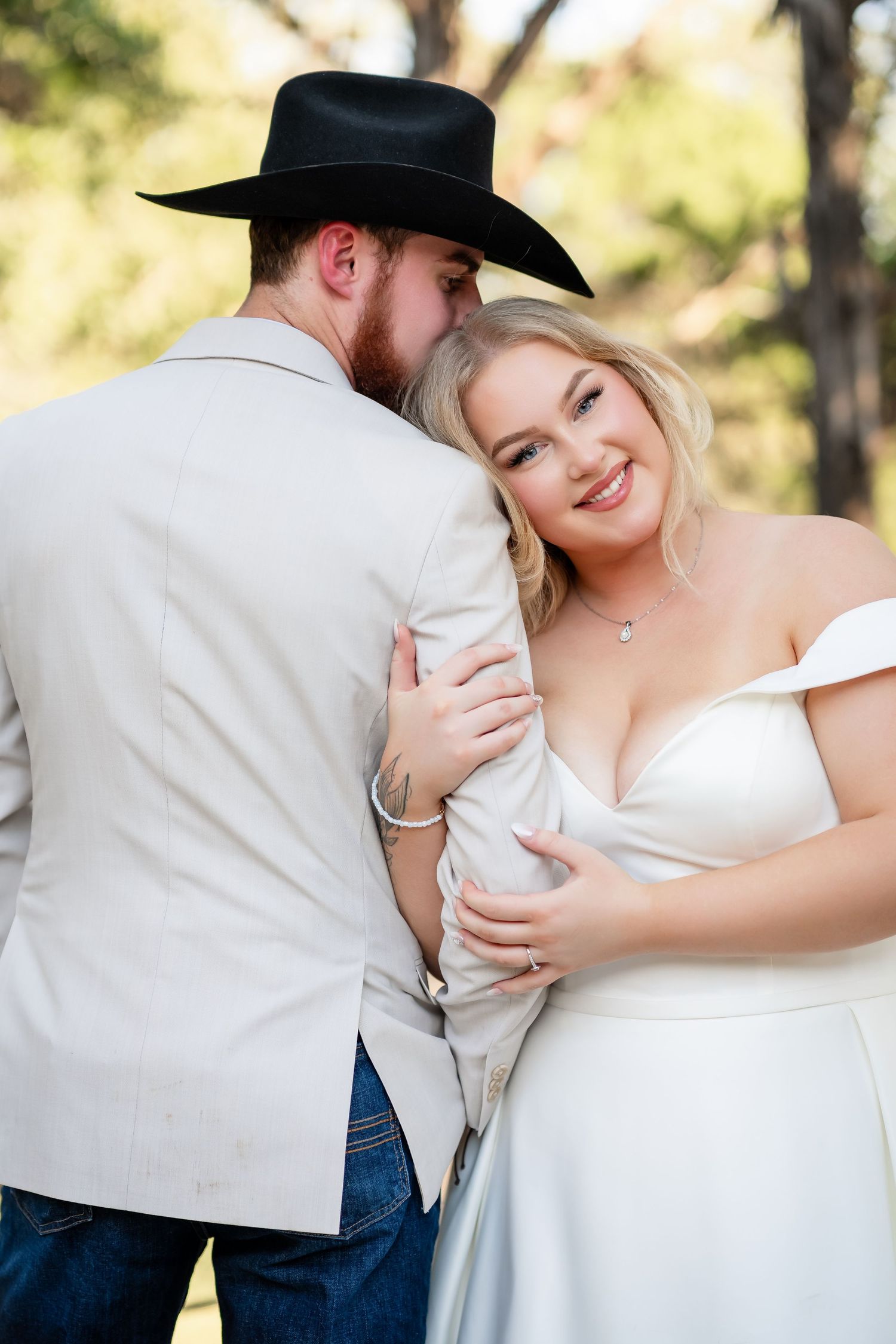Romantic wedding couple embracing outdoors with groom in cowboy hat and bride in white dress.