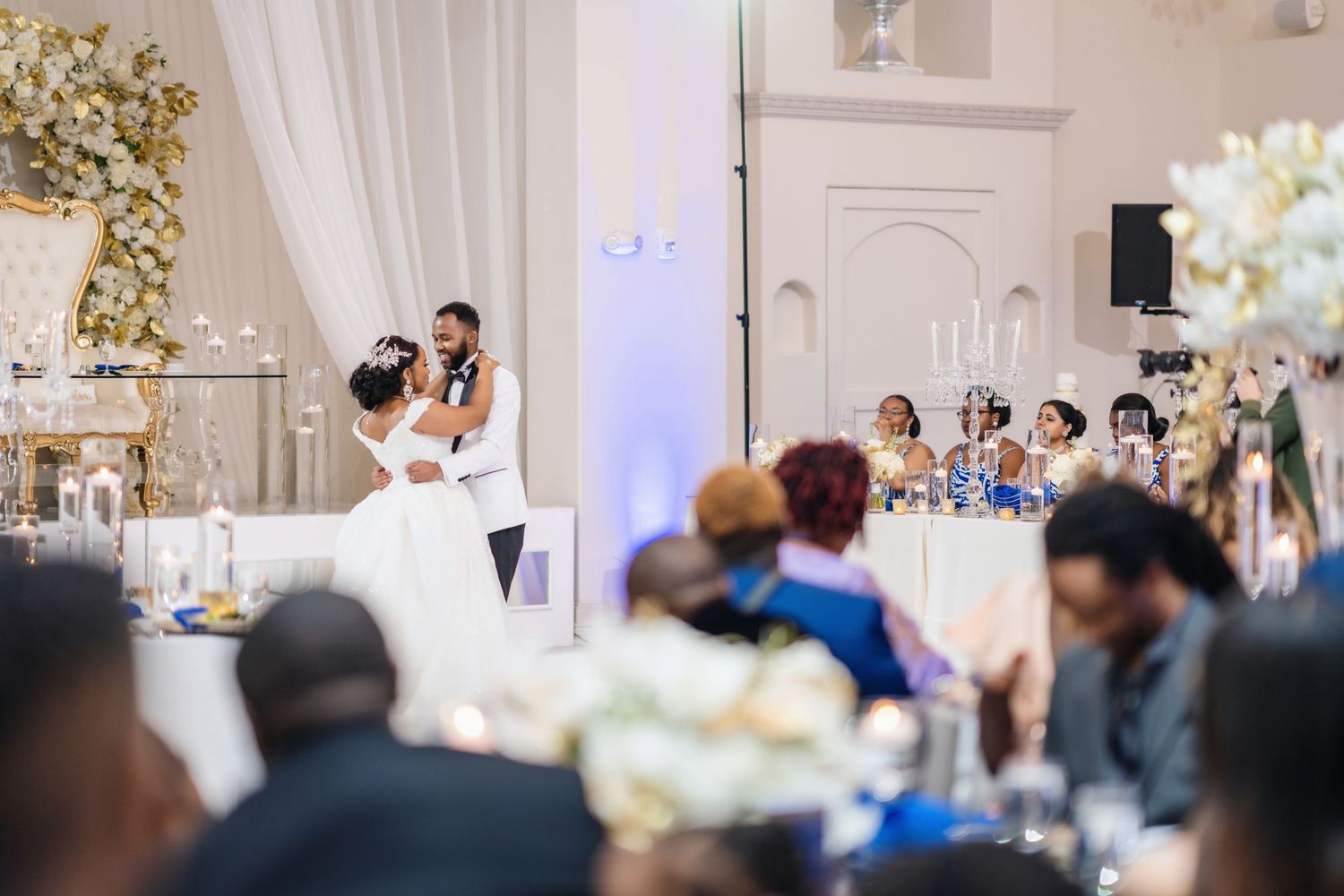 An elegant wedding reception venue decorated in white and gold with tables and floral arrangements.