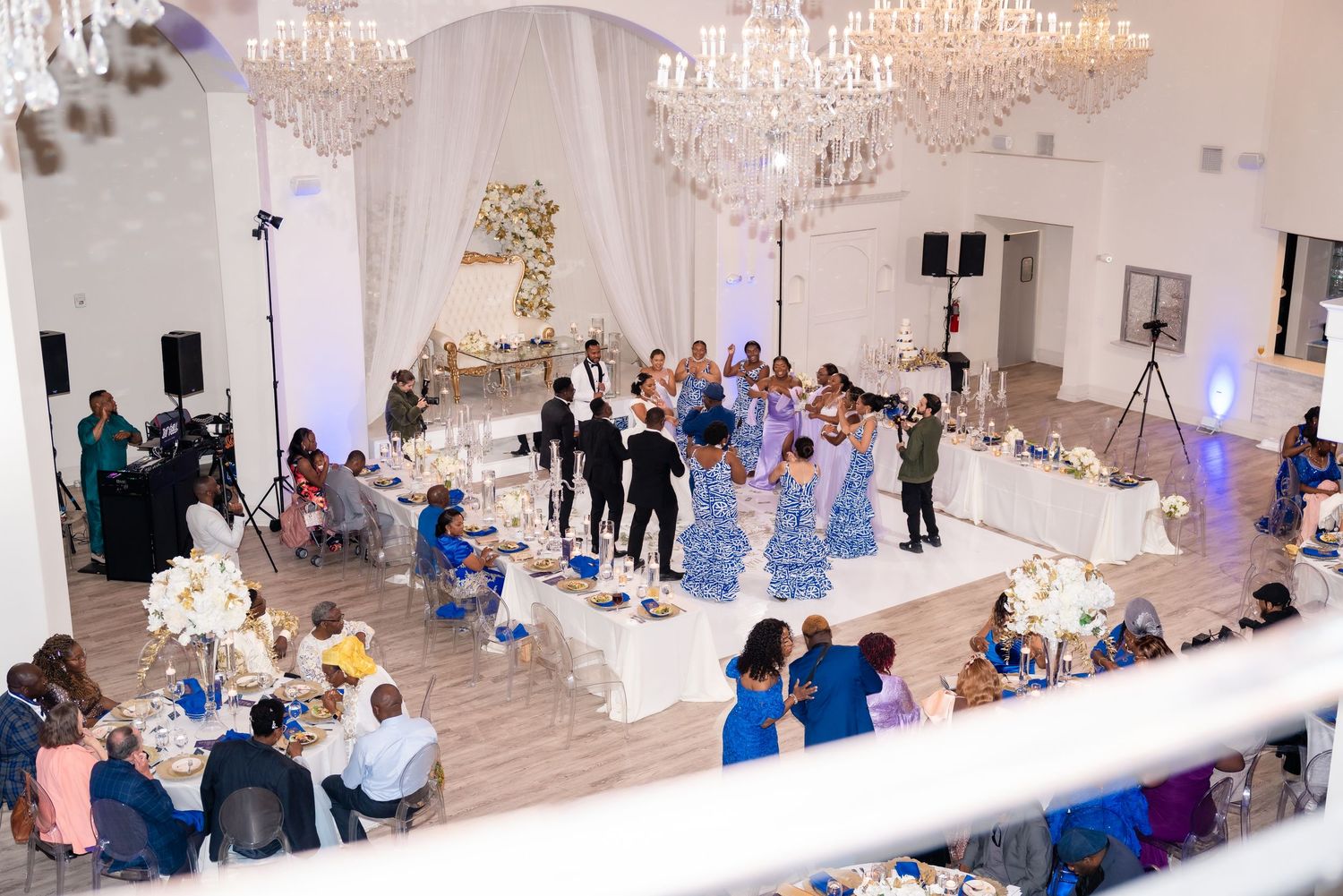 Grand ballroom reception setup with crystal chandeliers and elegant white draping along tables.
