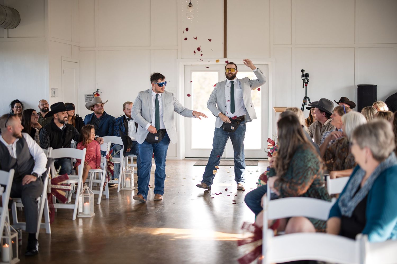 Wedding reception guests dance and celebrate inside a rustic indoor venue.