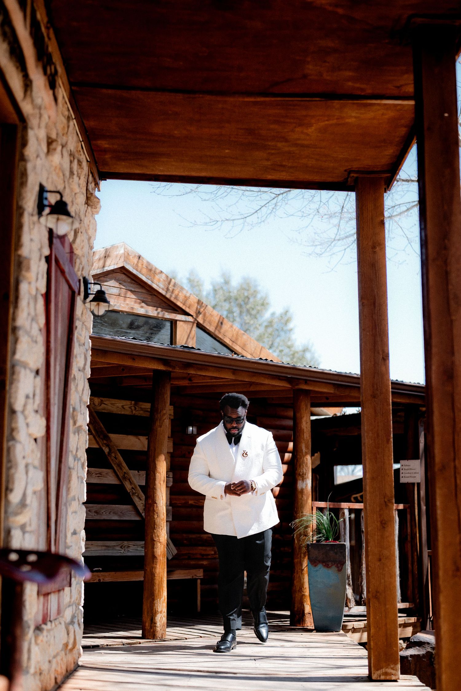 A person in formal white attire walks along a covered wooden porch at a rustic venue.