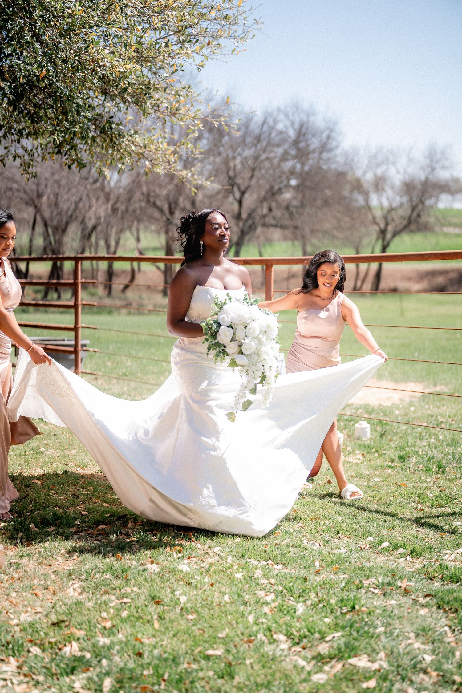Wedding dress flowing in the breeze as couple takes photos on grassy lawn with trees in background.