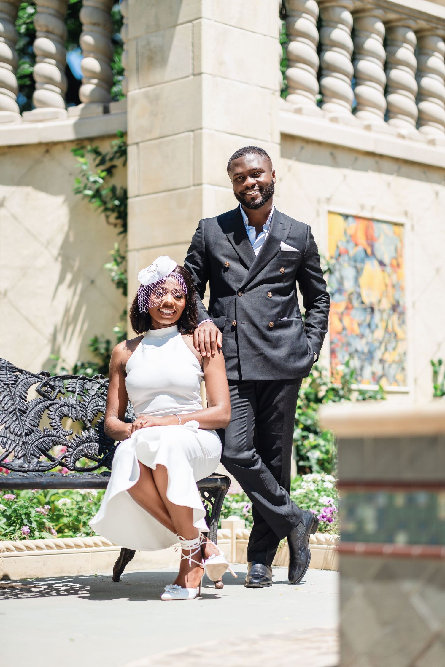 Elegant couple sits on stone steps with decorative mural and landscaping in background.