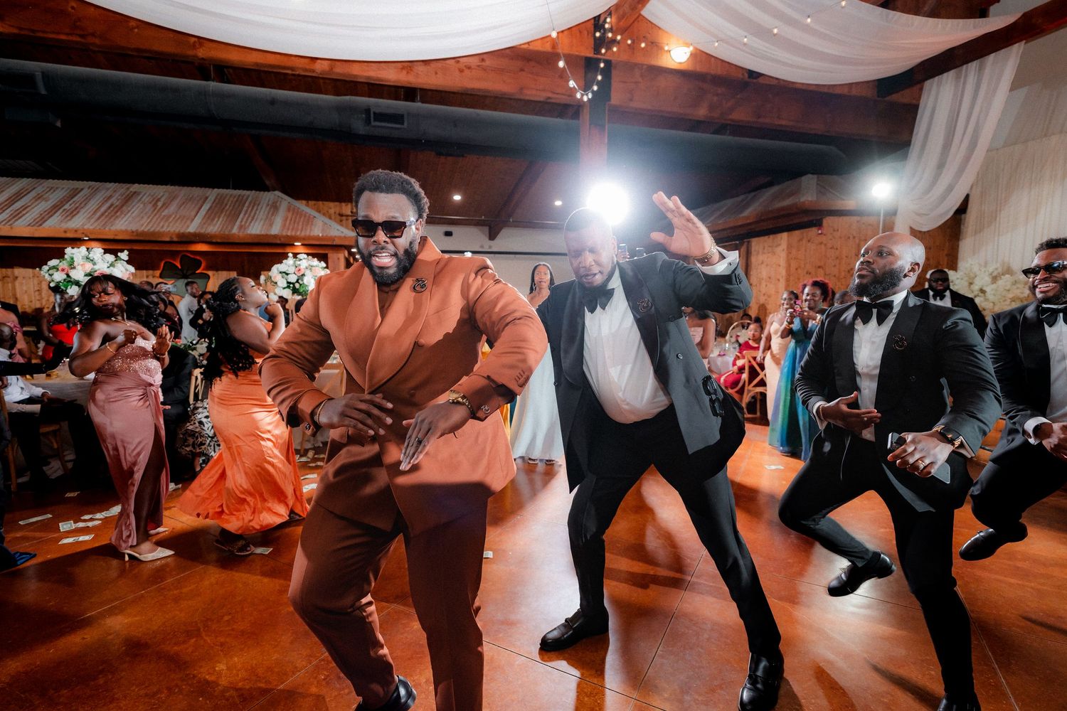 Wedding party performs choreographed dance routine on wooden dance floor.