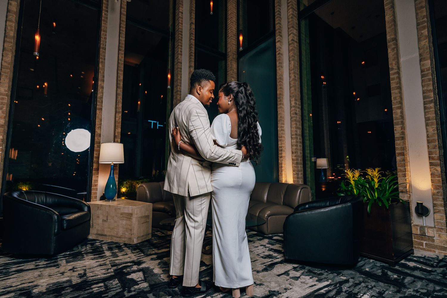 Couple in coordinated evening wear poses beneath illuminated columns.
