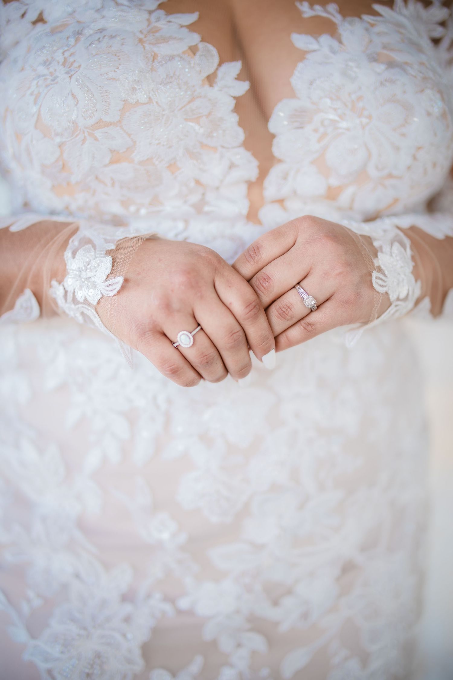 Close-up details of intricate lace patterns on a wedding dress with an engagement ring visible.