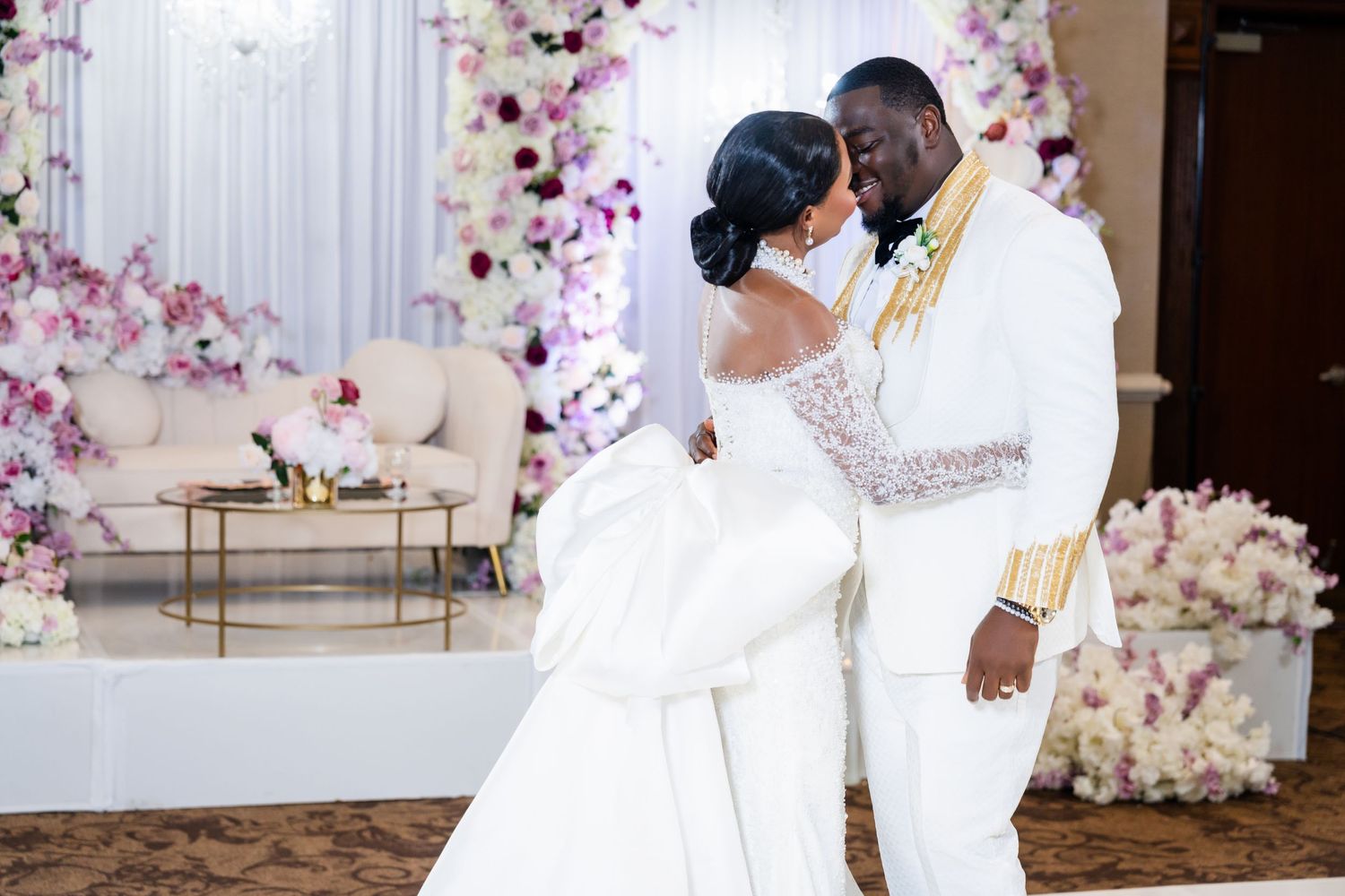 A romantic wedding scene with pink floral decorations and a couple sharing a tender moment in white attire.