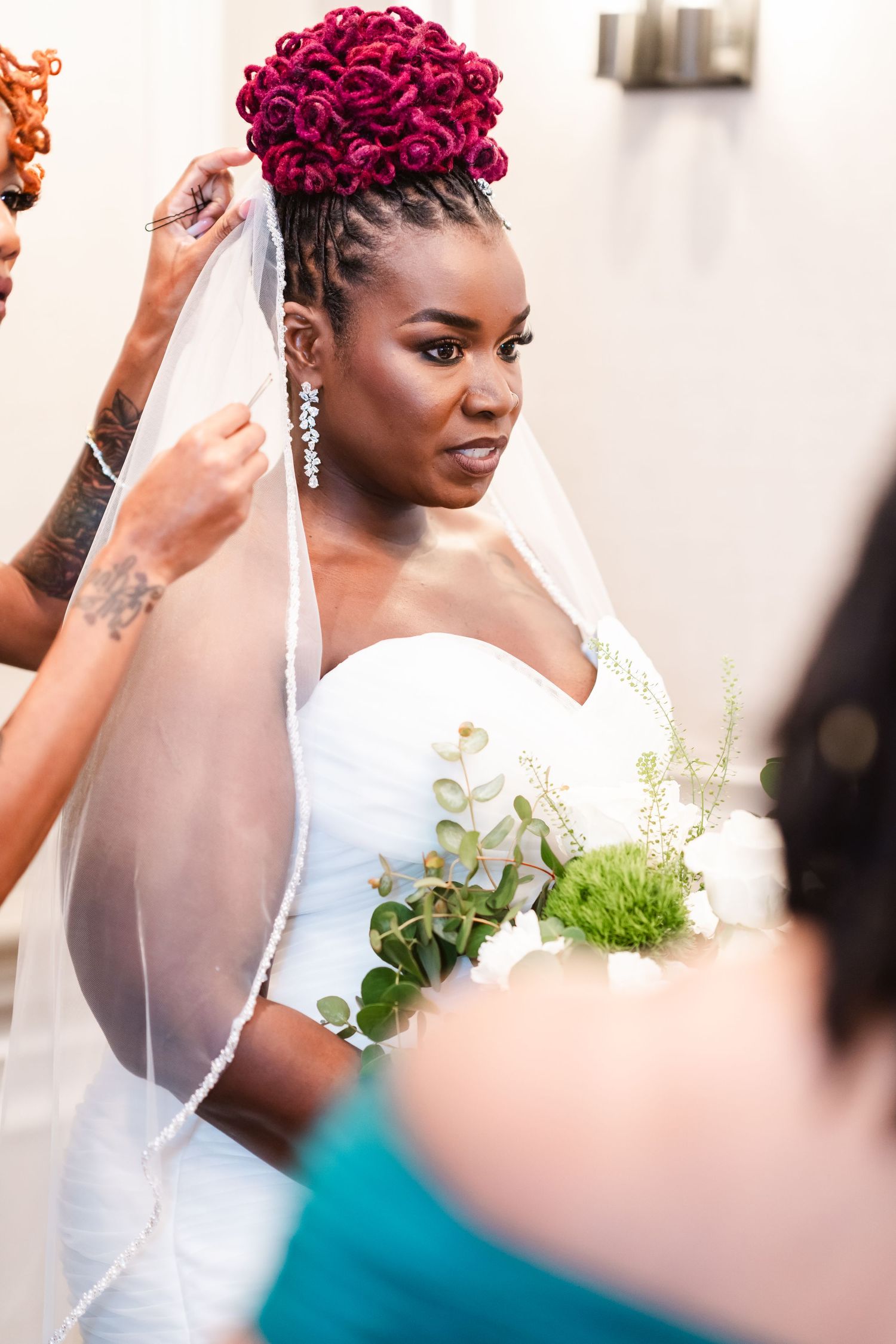 Beautiful bride wearing a white strapless gown with burgundy braided updo and veil holding a green and white bouquet.
