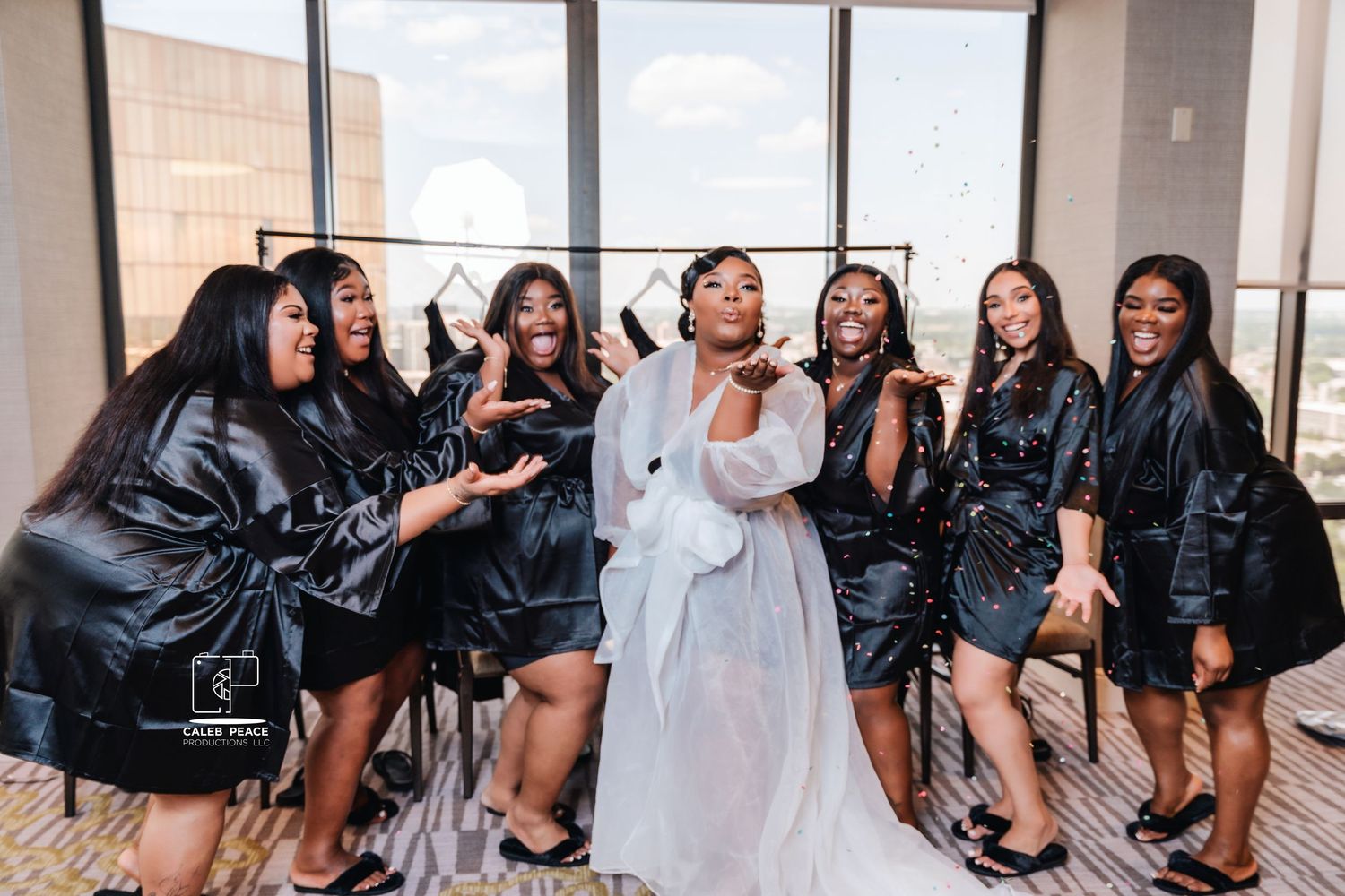 Bridesmaids in black dresses pose playfully together during wedding party photos.