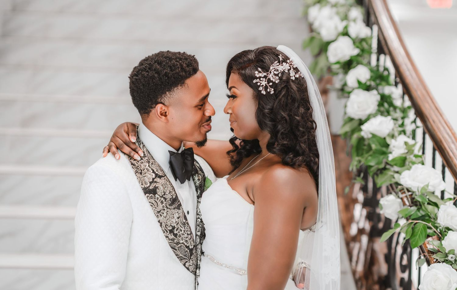 Close-up wedding portrait showing tender embrace against elegant white backdrop with floral accents.