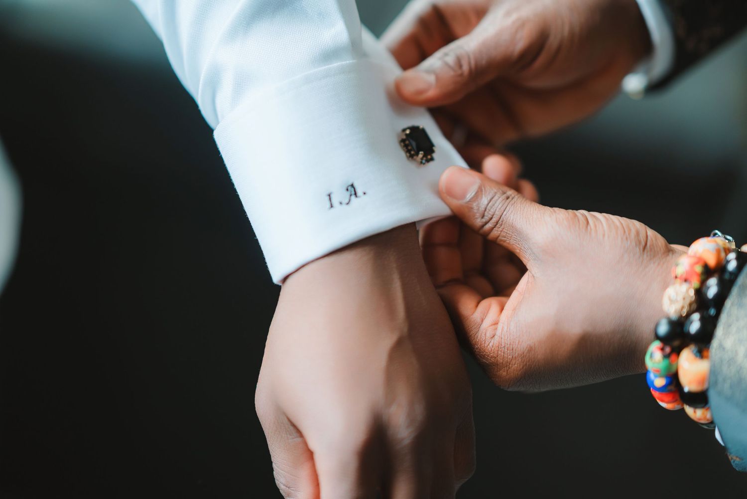 Close-up of hands adjusting formal white shirt cuffs with decorative cufflinks.