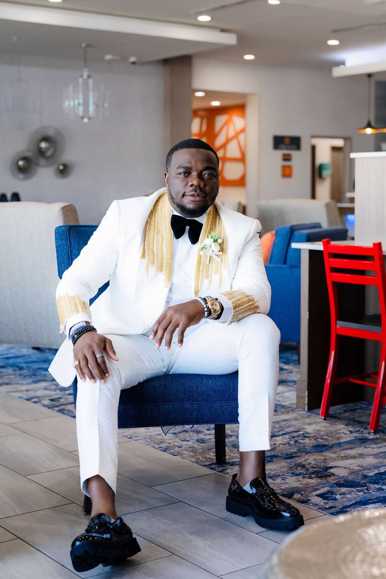 A person in white attire and black shoes poses on a blue couch in an indoor setting.