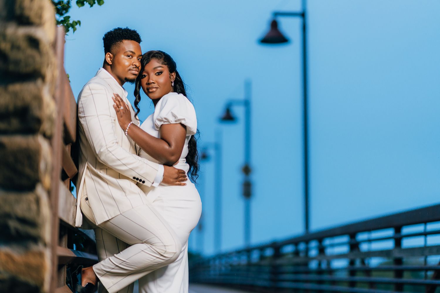 A couple embraces in an intimate dance pose against a blue sky and waterfront backdrop.