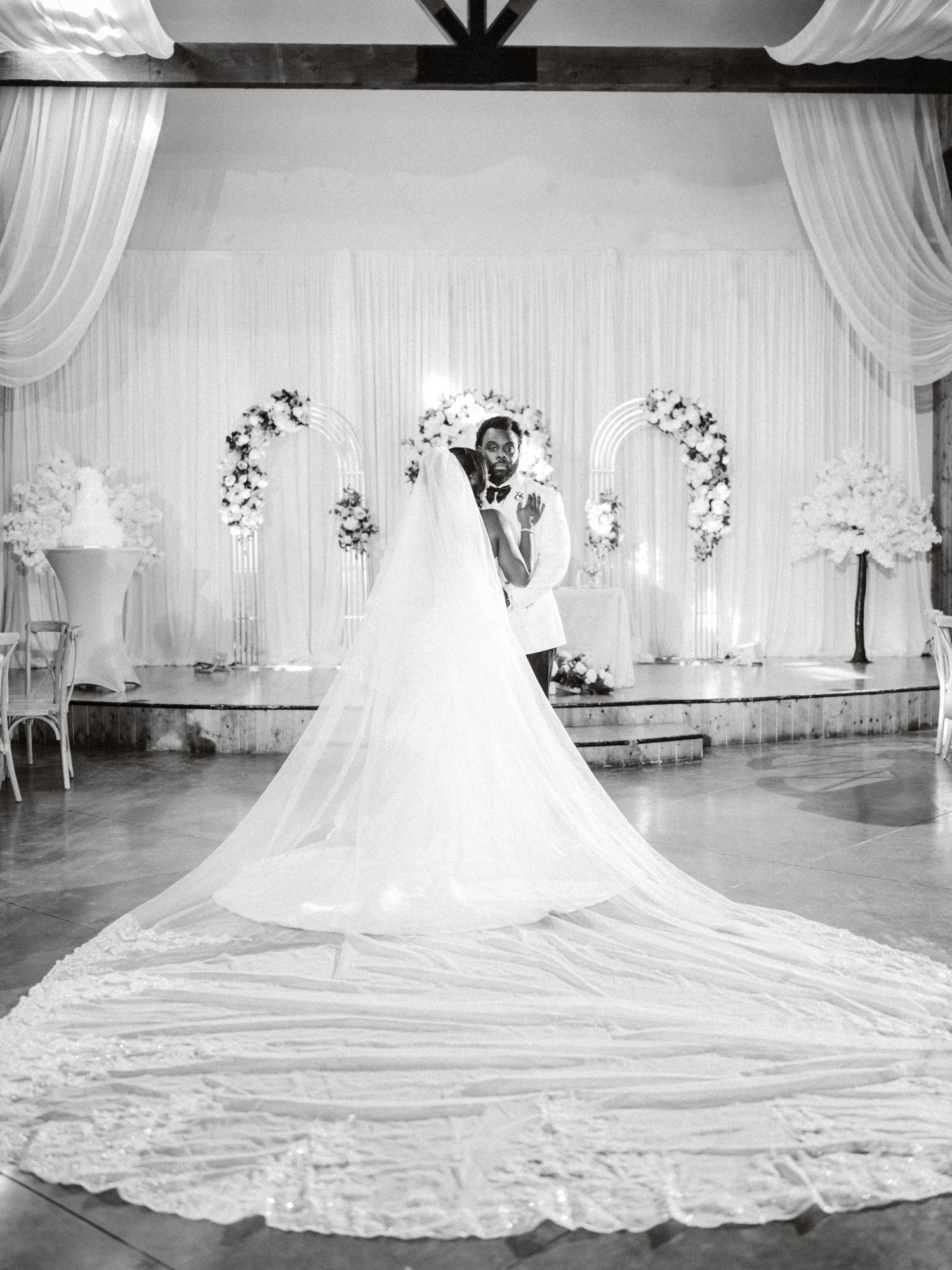 Stunning cathedral-length wedding dress train flowing across an elegant white-draped venue floor.