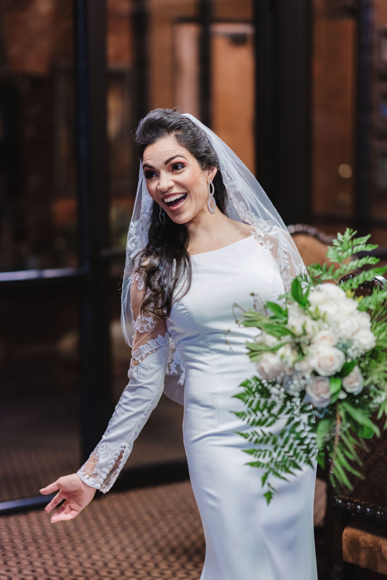 Bride in a classic white gown holds a lush green and white bouquet while posing playfully.