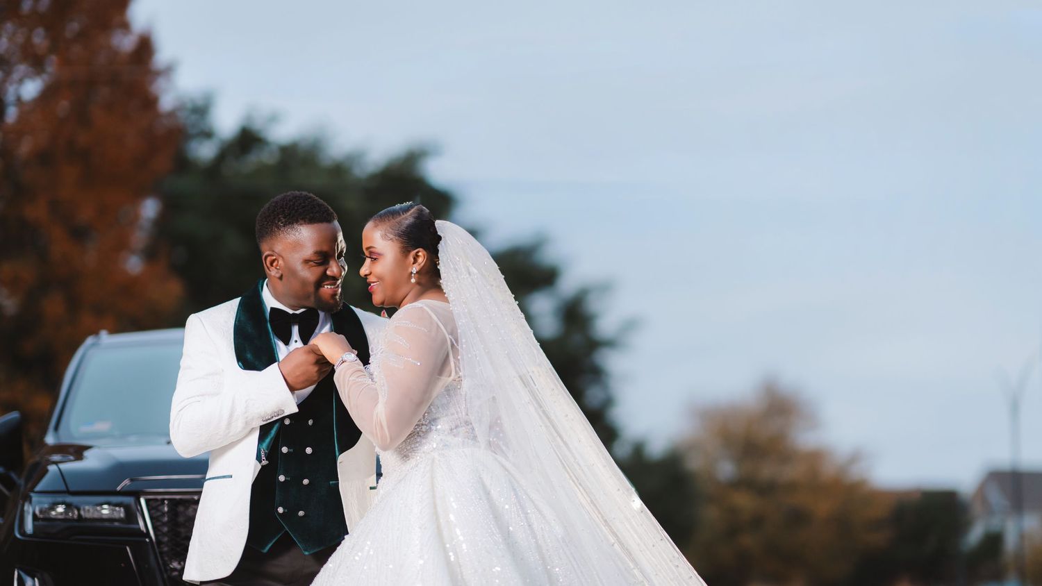 A couple in wedding attire embrace on a path with autumn trees in the background.