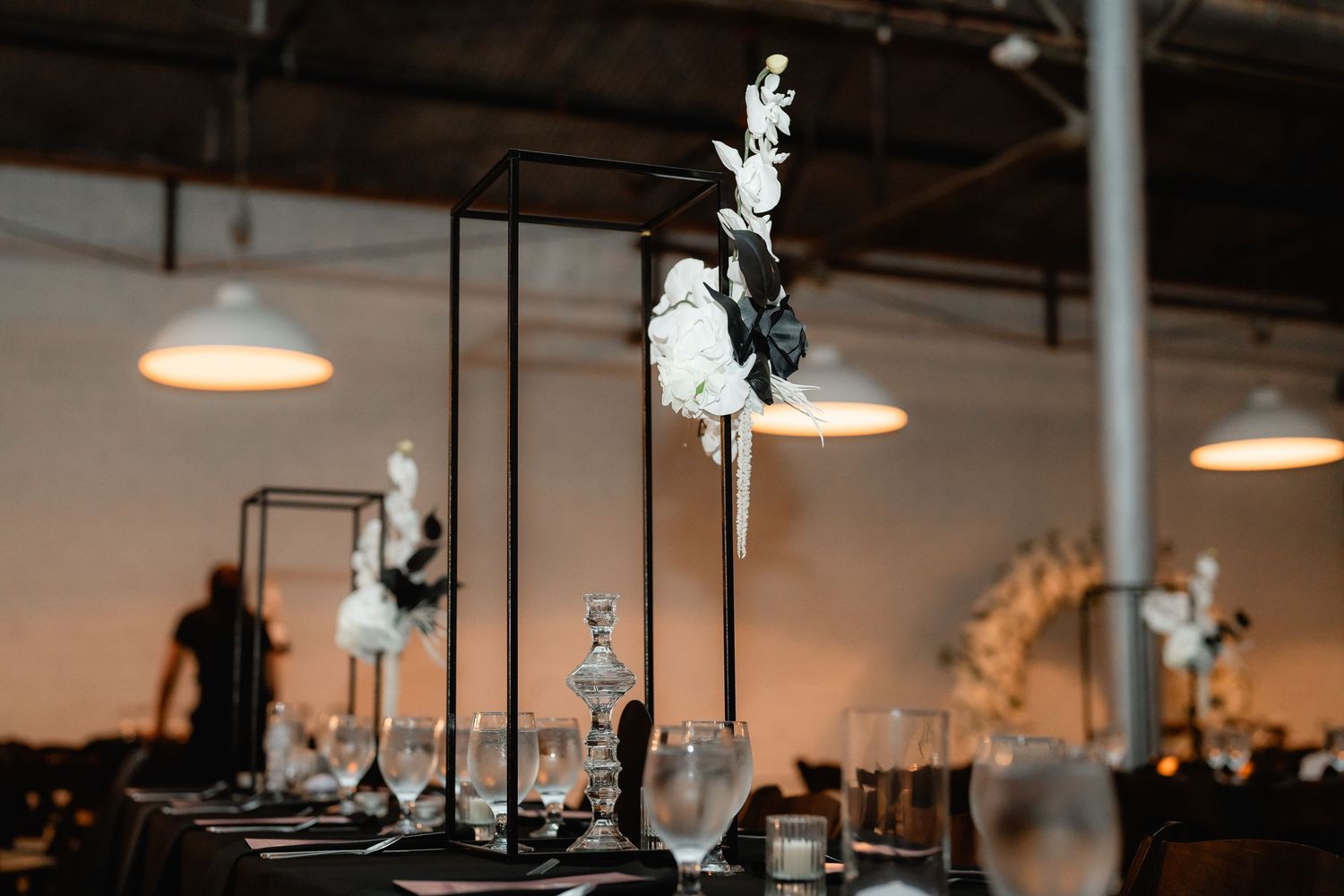 Modern wedding decor features minimalist black pedestals with white floral arrangements.