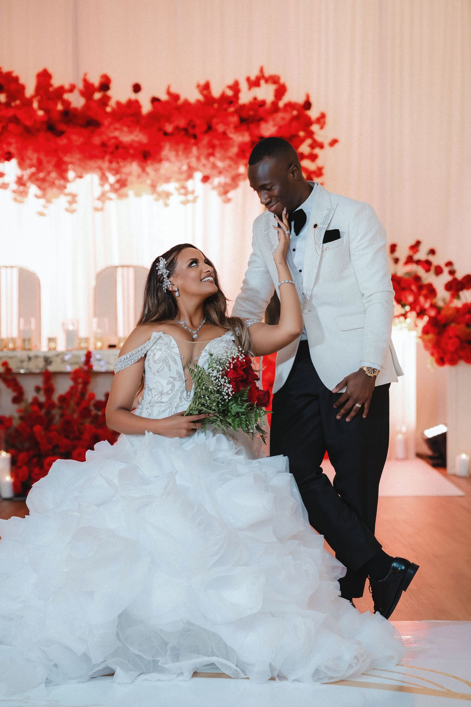 A romantic wedding photoshoot with a couple posing against a backdrop of red floral decorations.