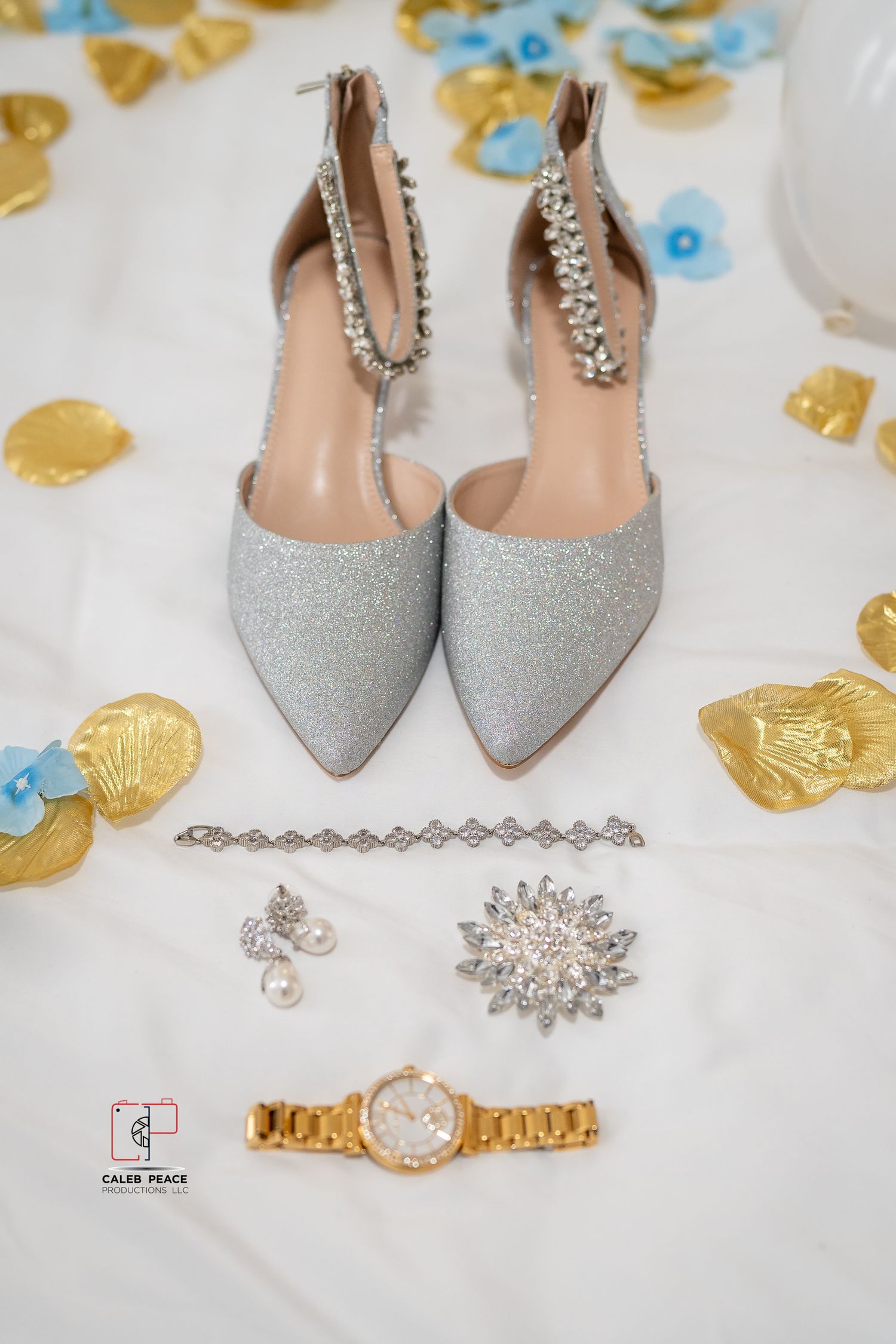 Sparkly silver bridal shoes and elegant crystal jewelry accessories arranged with gold and blue floral petals.