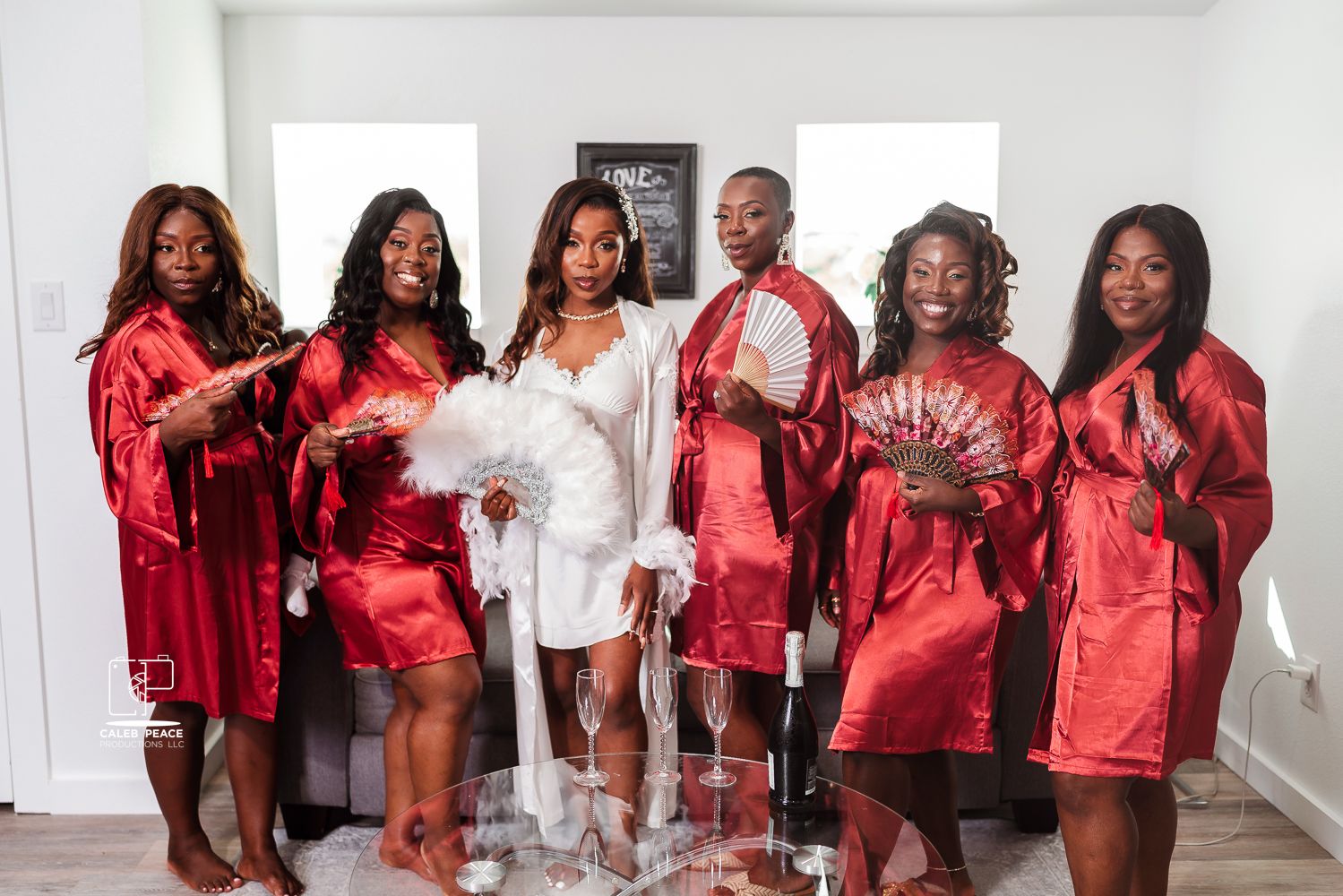 Wedding party wearing matching red satin robes posing in white room.