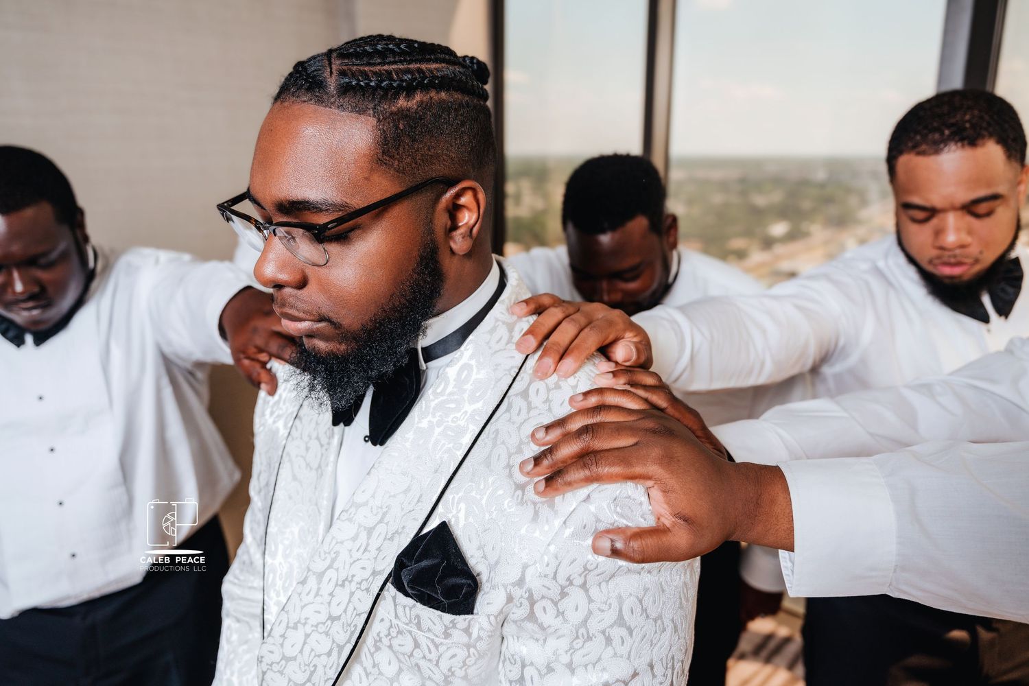 Group of groomsmen in matching white jackets embracing during wedding preparations.