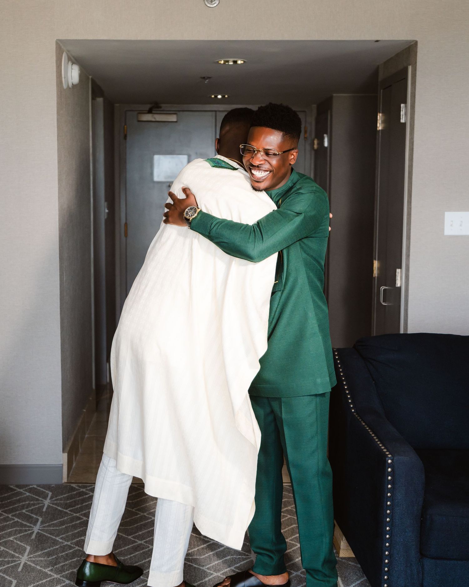Person in green suit adjusting white clothing in a hotel hallway.