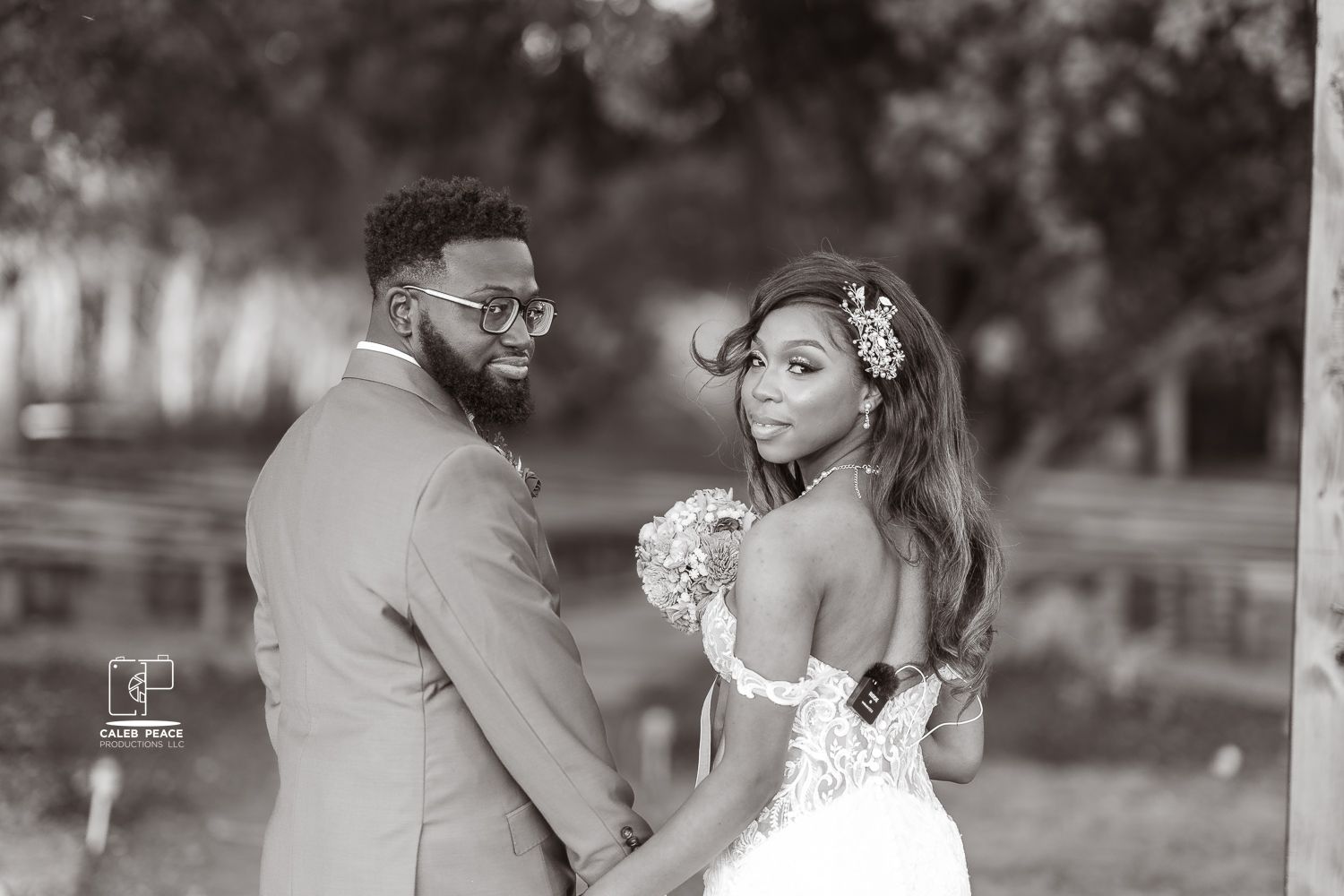 A romantic black and white wedding photo shows a couple outdoors, with the bride holding a bouquet and wearing a backless dress.