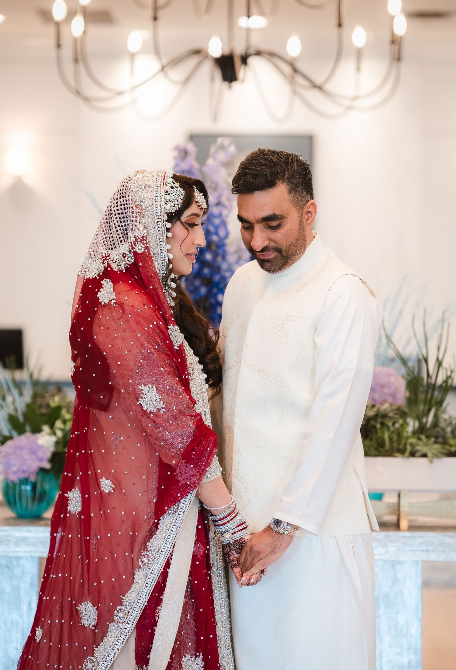 Couple in traditional South Asian wedding attire standing together in an elegant indoor setting.